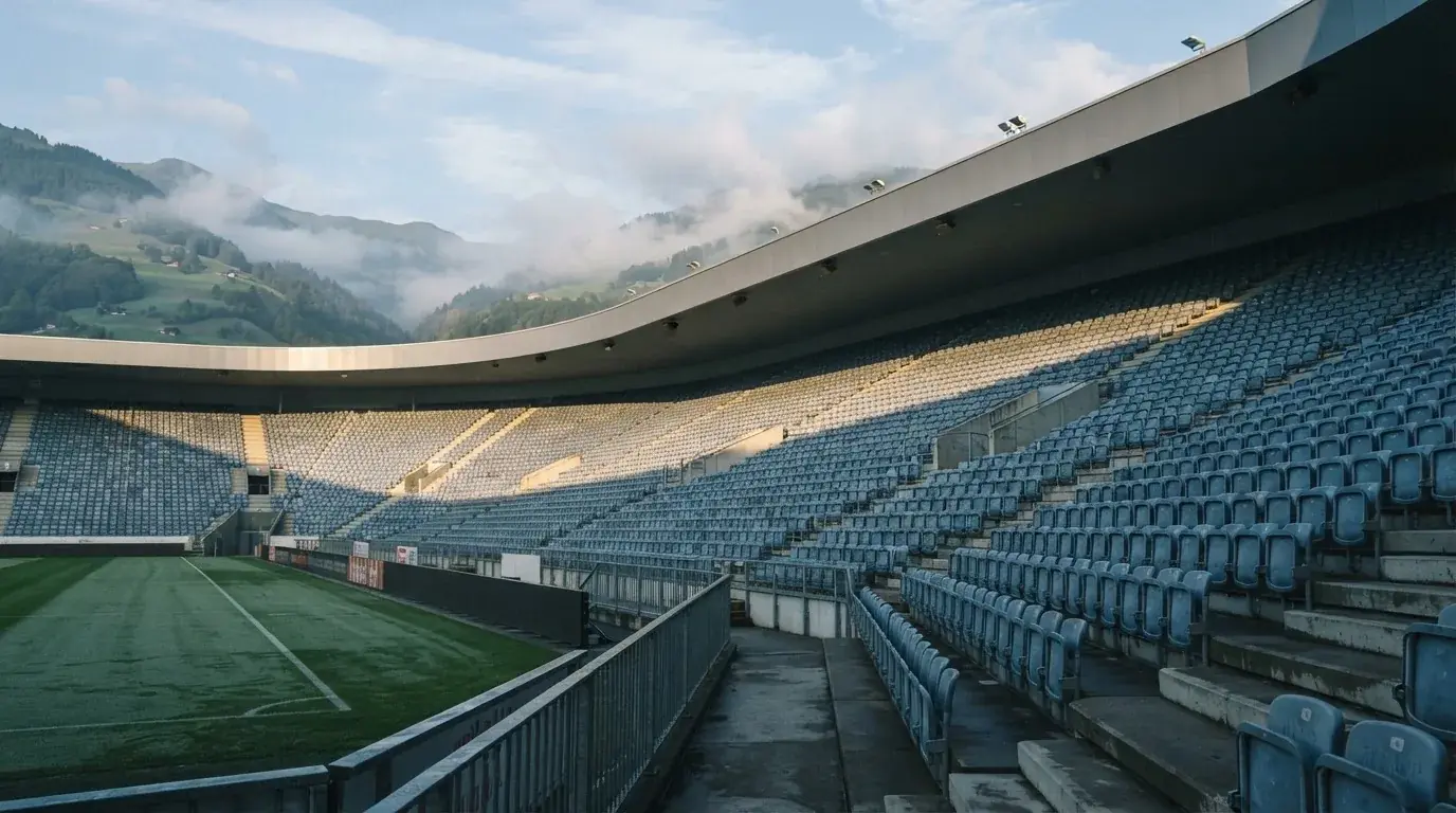 Ein leeres Stadion im Morgenlicht mit Blick auf die Sitzreihen, im Hintergrund Hügel und aufsteigender Nebel.