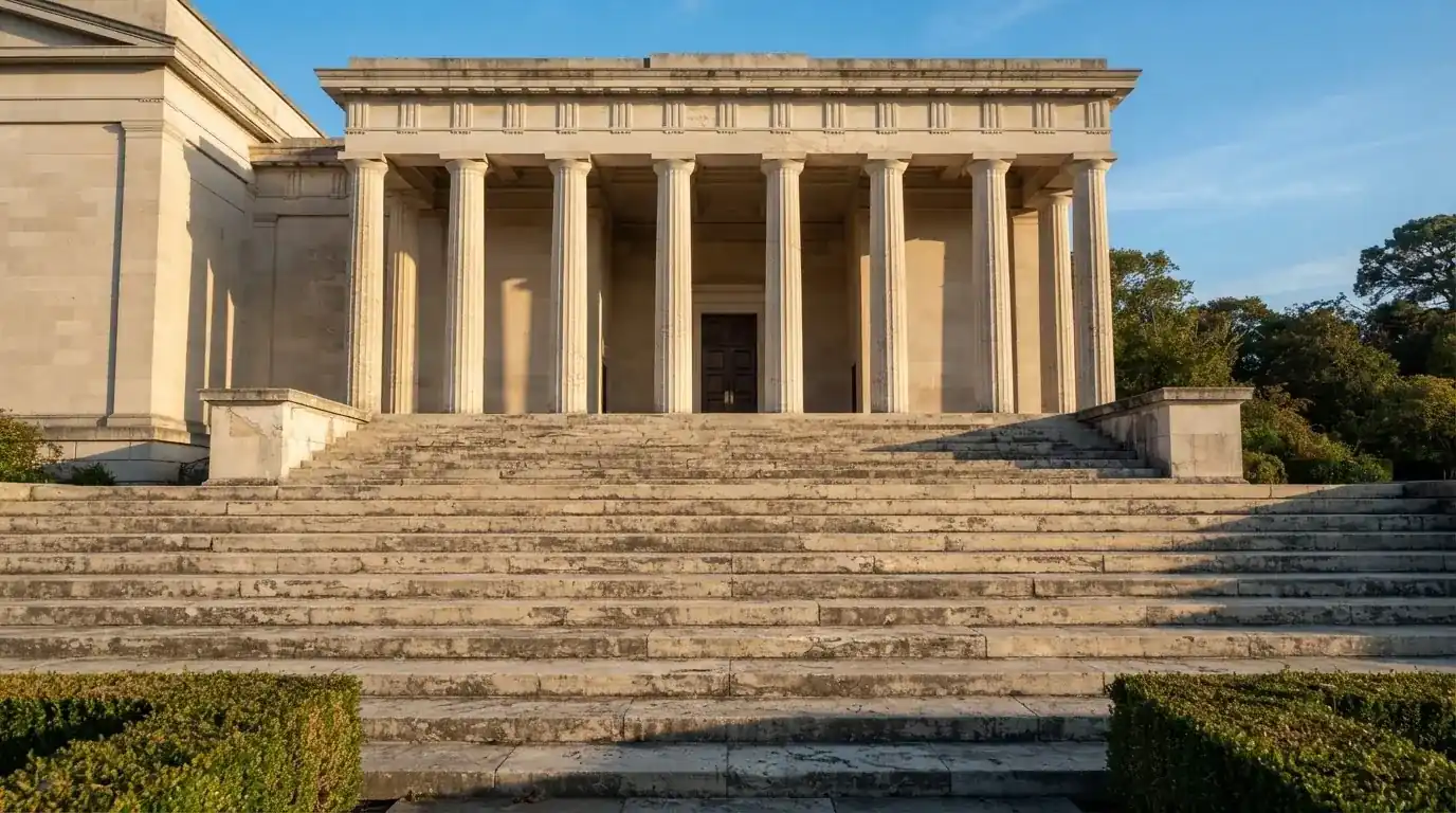 Eine breite Steintreppe führt zu einem Gebäude mit Säulen, die Morgensonne scheint, niemand ist zu sehen.