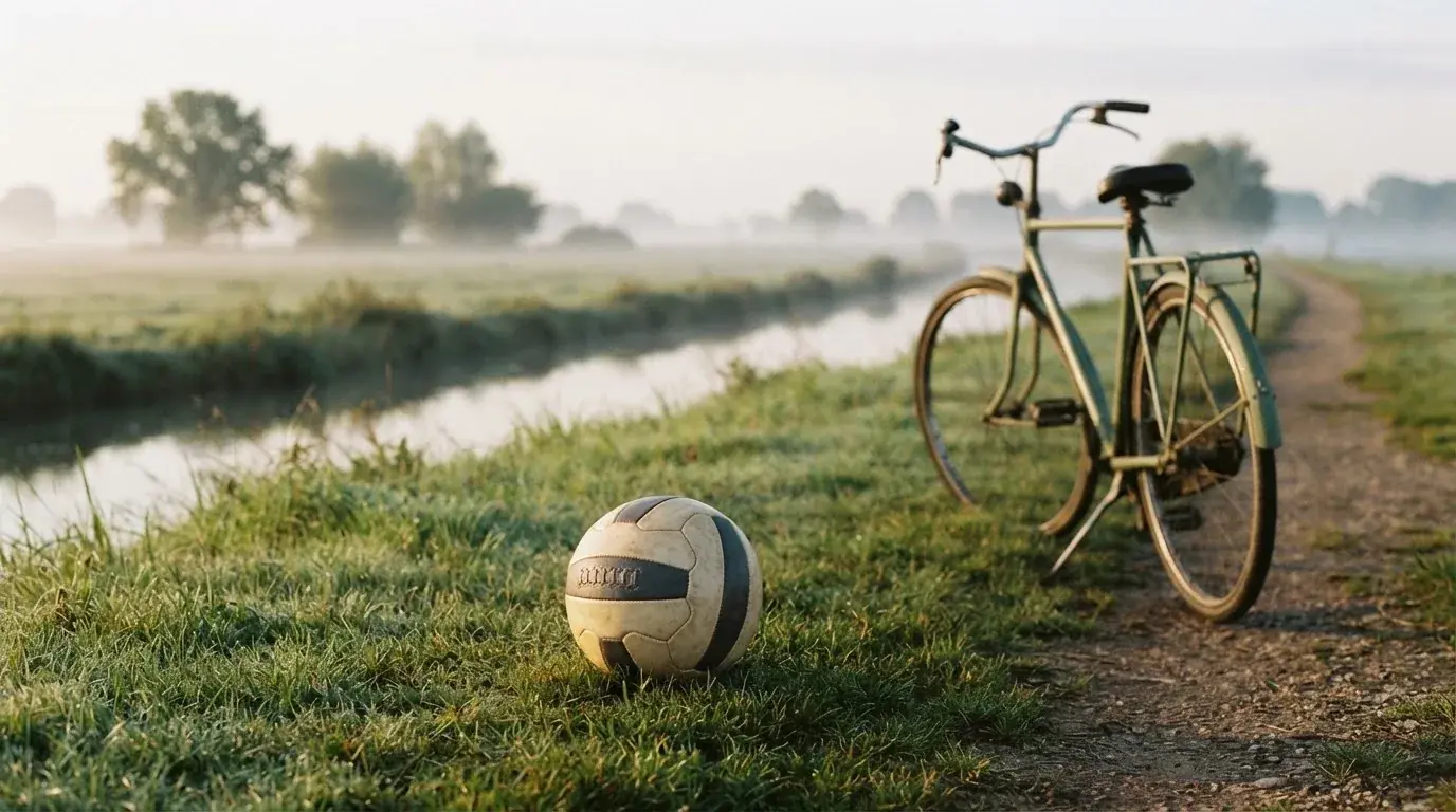 Ein Fussball liegt auf einer Wiese neben einem Fahrrad, im Hintergrund ein Kanal im Morgenlicht